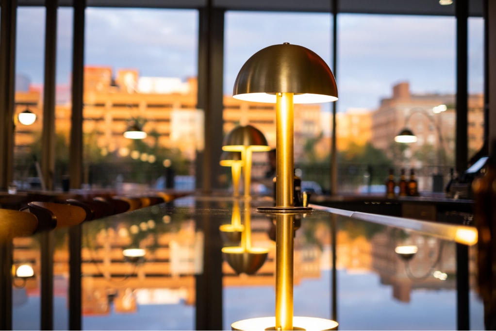 Domed brass lamps on top of a black bar top in front of floor-to-ceiling windows