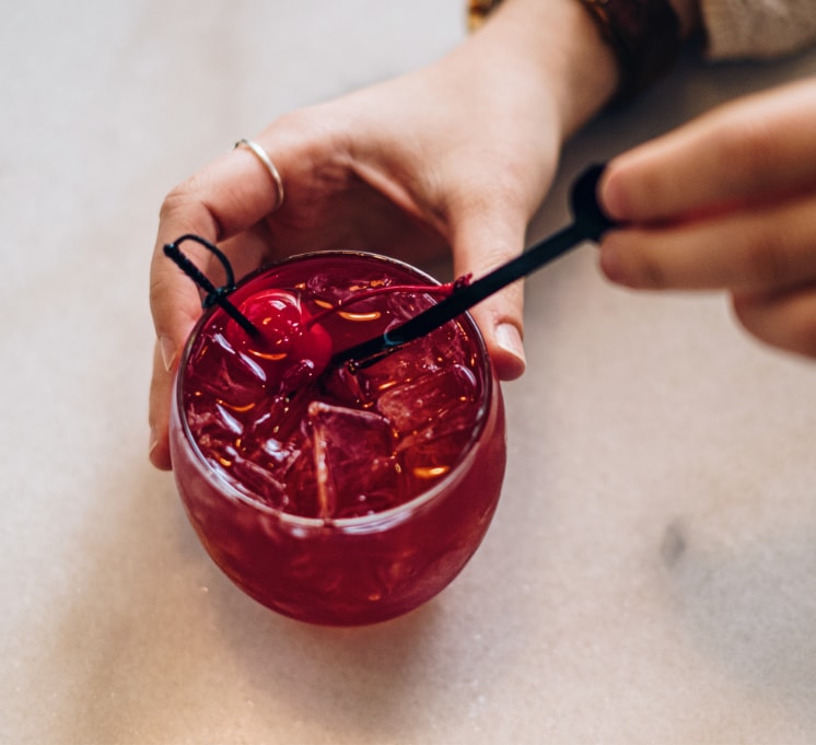 A hand holds the deep red Old Fashioned cocktail and places it gently on a marble tabletop.