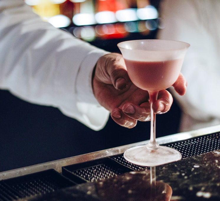 A bartender picks up the pastel Pink Squirrel cocktail in a frosted glass