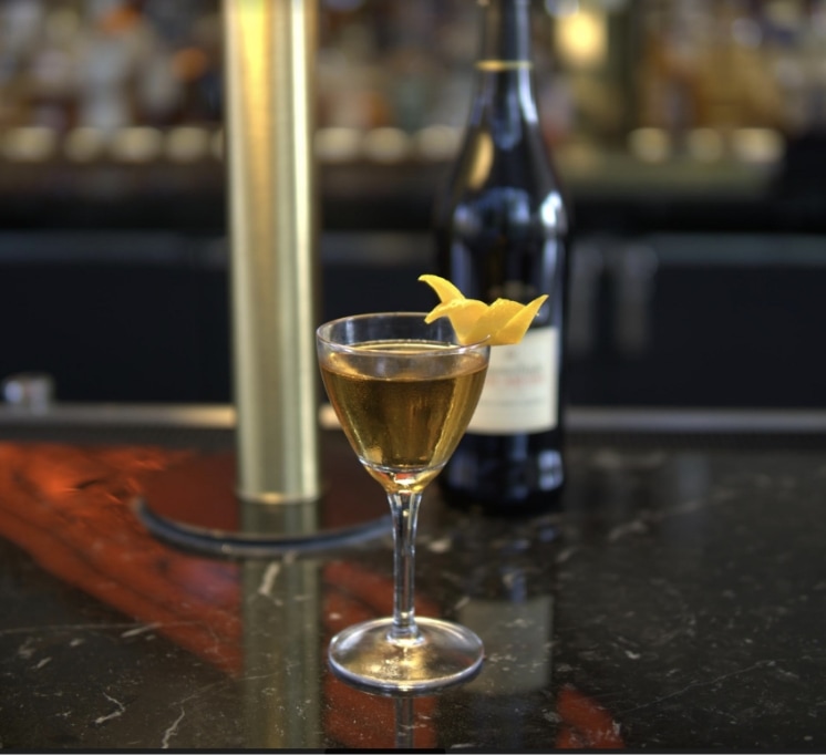 A cocktail with a lemon twist sits on top of Hammer and Nails black marble bartop